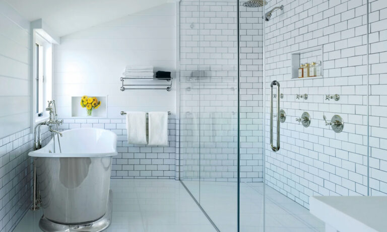 Spacious and modern bathroom featuring a freestanding vintage-style tub, glass shower enclosure, white subway tile walls, and stylish fixtures. A vase of sunflowers adds a pop of color, complemented by neatly arranged towels and a minimalist design.