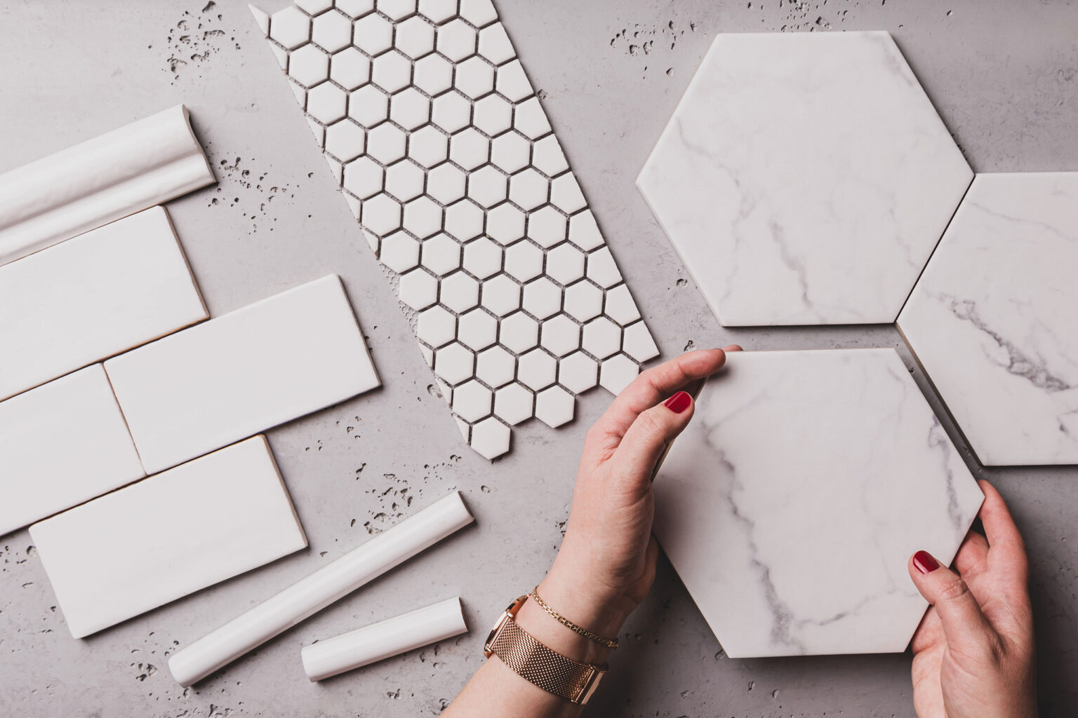 Hexagonal marble tile among various white ceramic tiles and a hexagon patterned tile on a gray surface, showcasing different tile designs for home renovation or interior decoration projects.