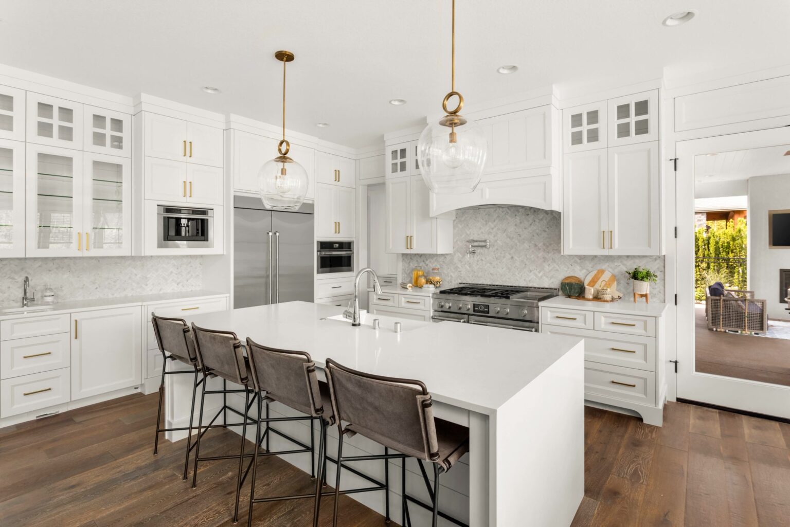 Modern kitchen featuring white cabinetry with gold hardware, a large island with seating, and pendant lighting. The design includes stainless steel appliances and a stylish backsplash, creating a bright and inviting space.