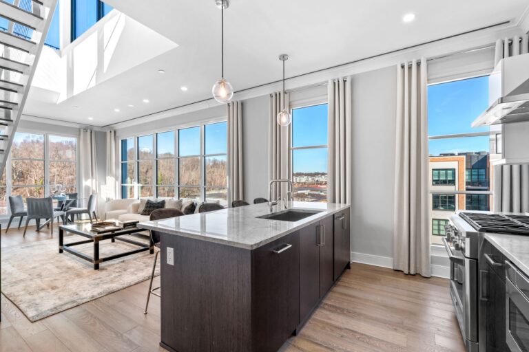Modern kitchen and living area in a bright, spacious apartment featuring large windows, stylish decor, and a sleek island with a marble countertop. The design emphasizes natural light and contemporary furnishings.