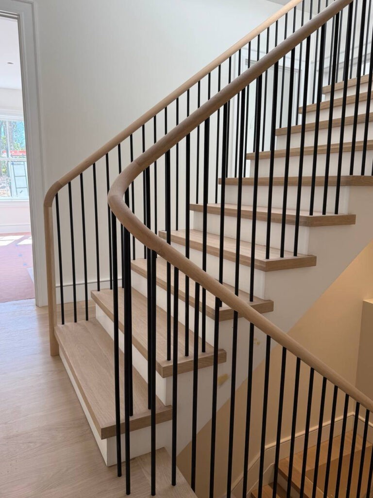 Modern spiral staircase with wooden steps and black metal railings, featuring a clean, minimalist design and natural light illuminating the space.