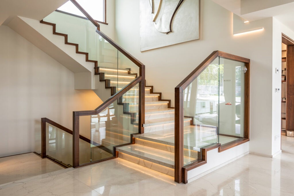 Modern staircase design featuring wooden steps with glass railings and integrated LED lighting, enhancing the contemporary aesthetic of the residential interior.